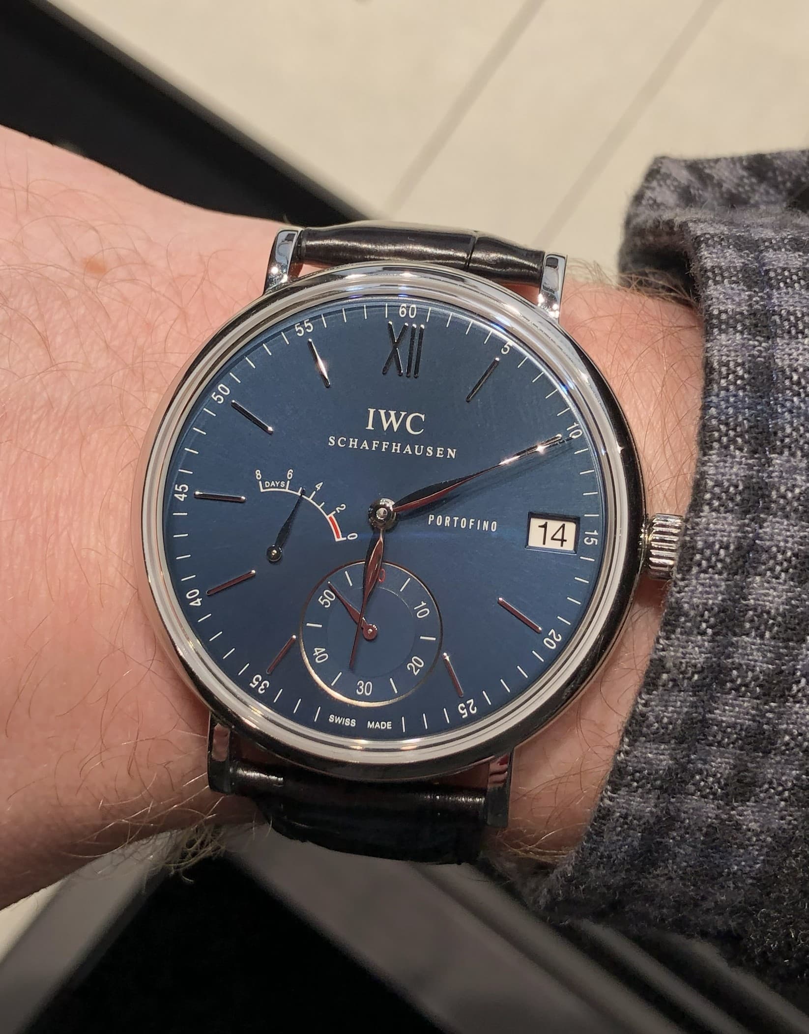 a blue IWC portofino 8-day power reserve with steel case on a black bracelet on a man's wrist.