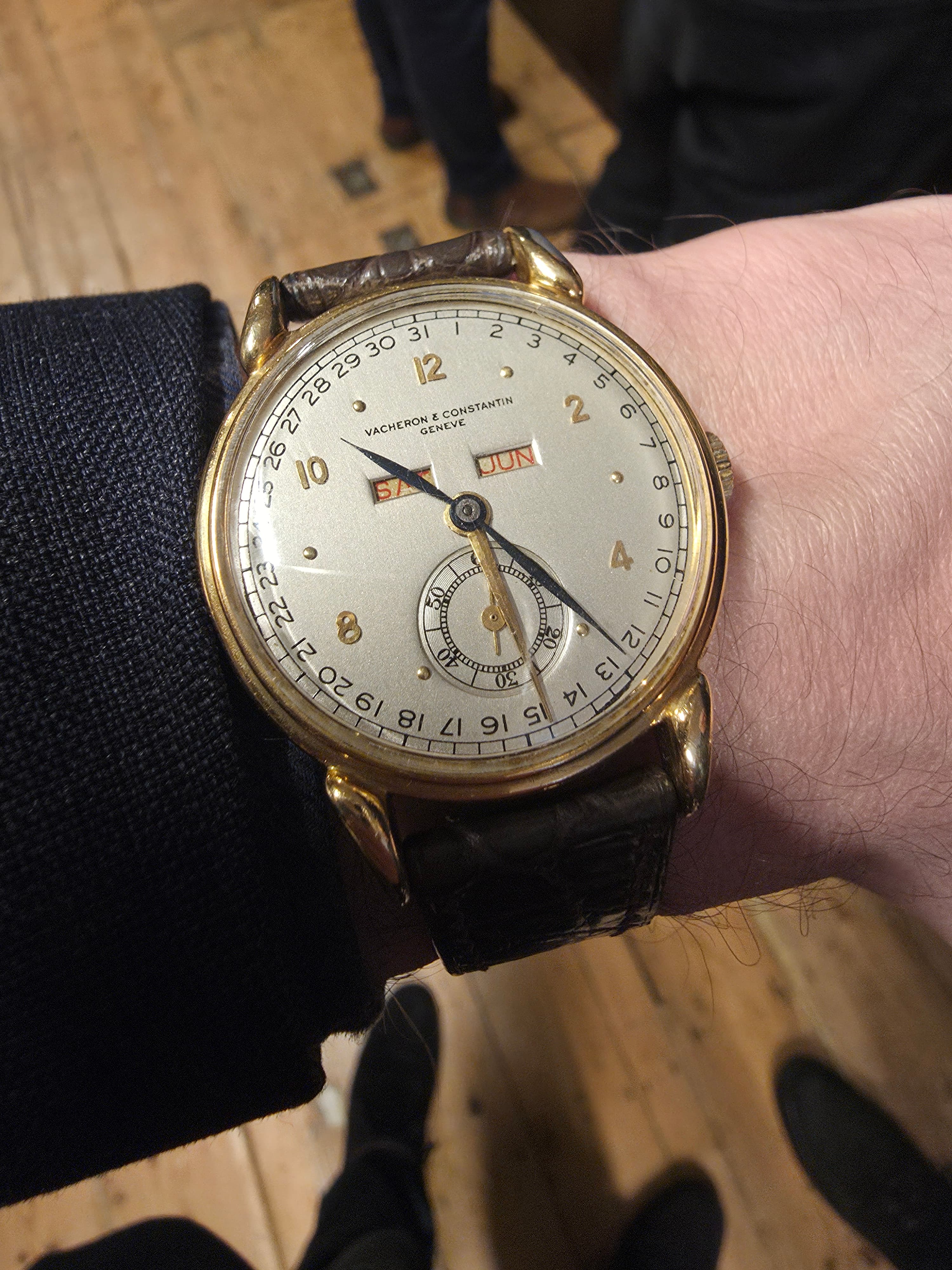 a beuatiful gold Vacehron Calendar constatin triple calendar wristwatch on the wrist in close up with white dial gold hands and case, red date and day markers and small subseconds at 6 o'clock