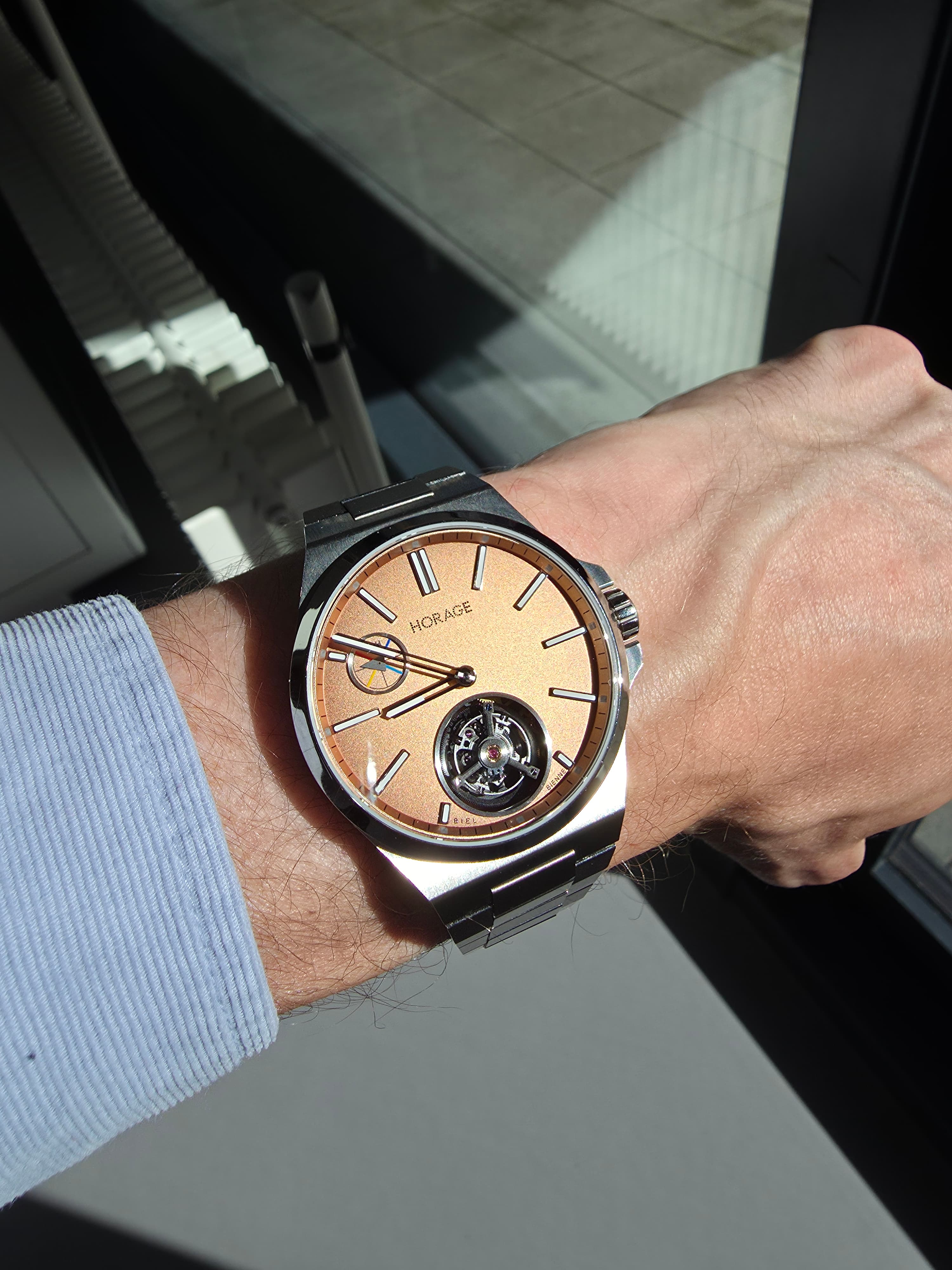 horage toubrillon watch with steel case and salmon dial and visible tourbillon cage at 6 oclock