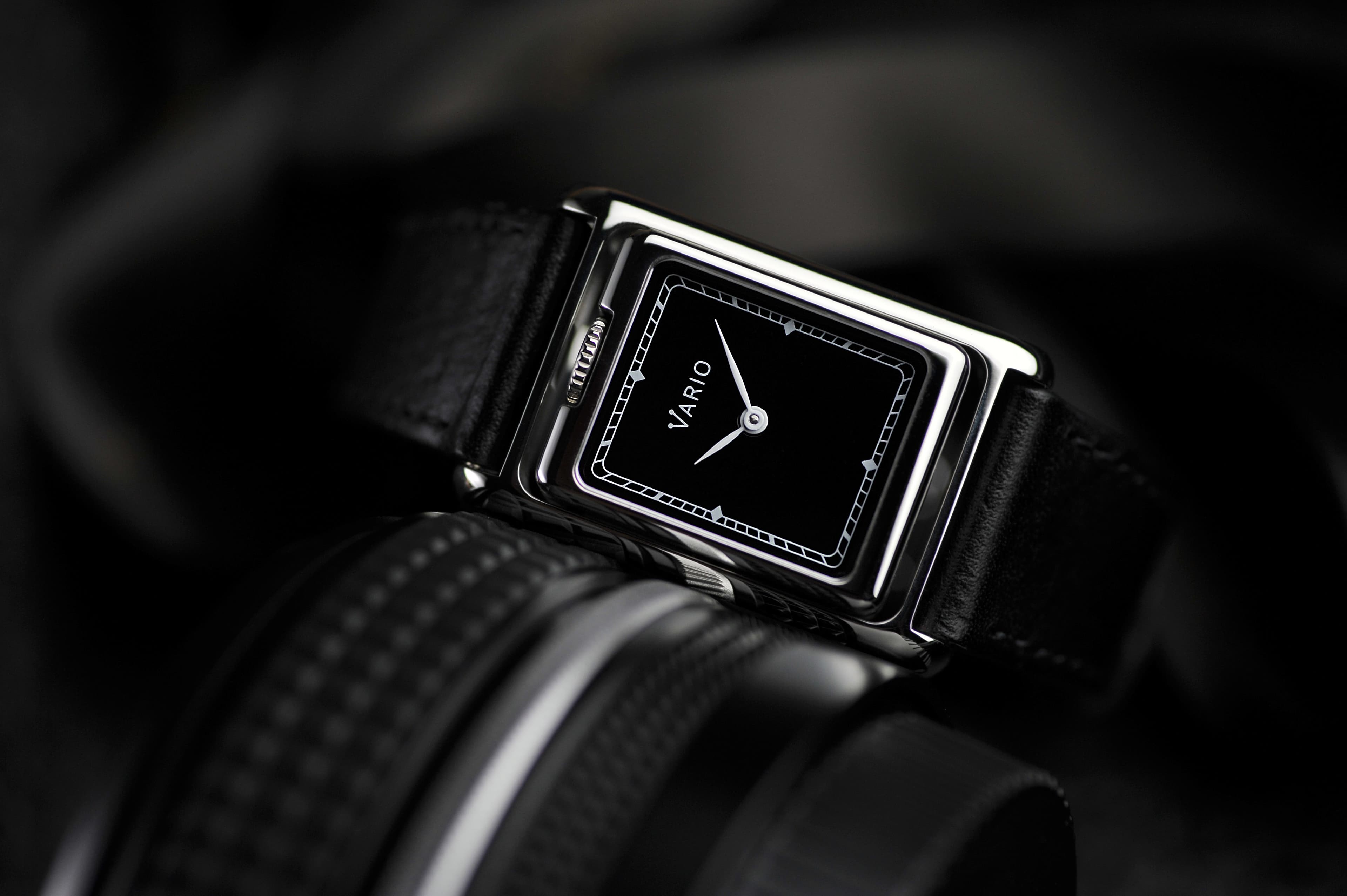 a black dial vario versa rectangular wrist watch with crown at the top and black leather band