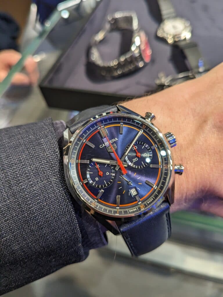 a dark blue TAG HEuer Carrera watche swith red and orange hands on a dark blue strap with other watches in the background at a watch event