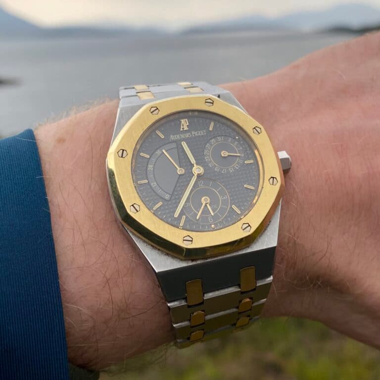 bimetal royal oak watch with gold besel steel case and grey fdial with gold hands on grey and gold bracelet on wrist with sea in thebackground
