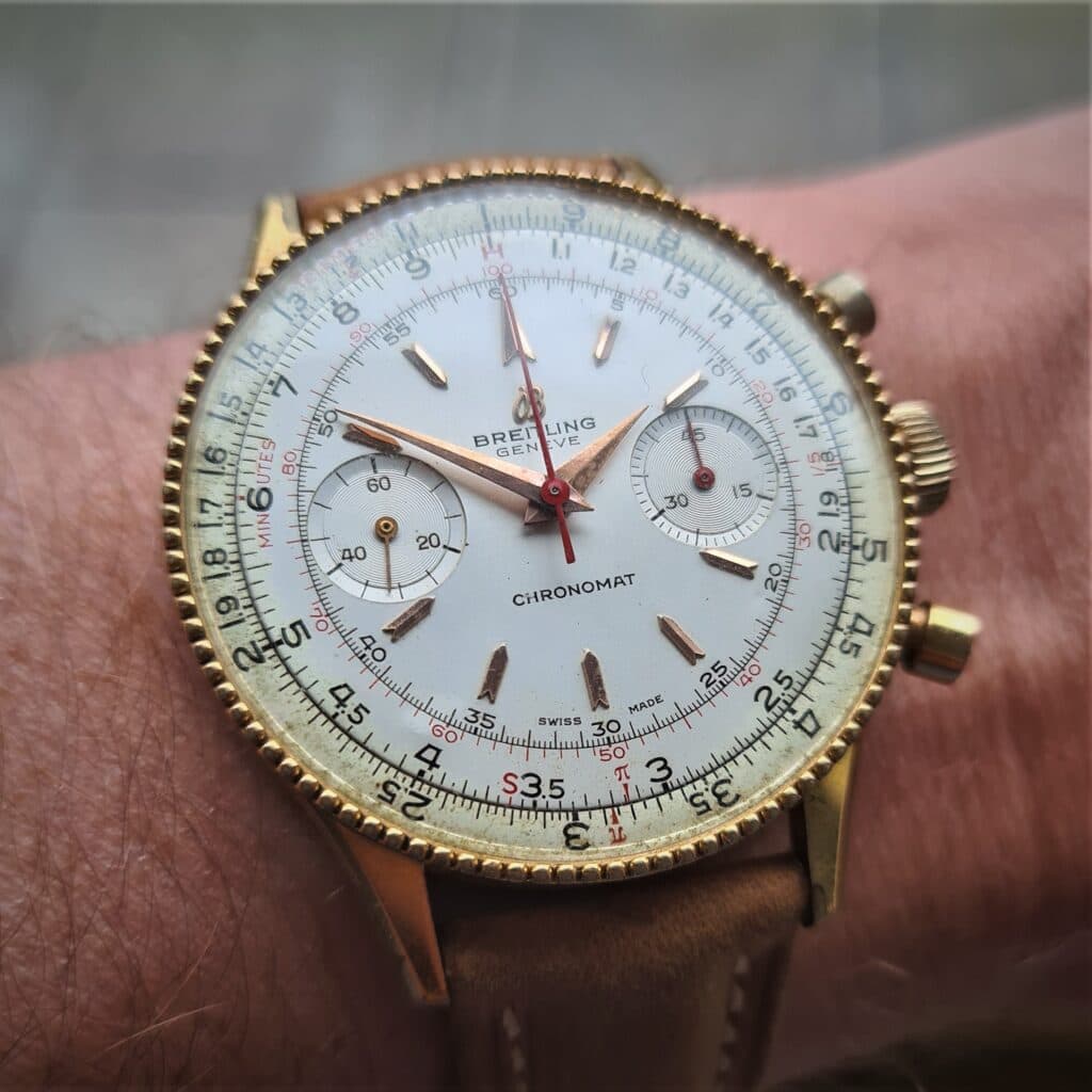 gold vintage breitling with white cream dial with gold dagger hands and red minute hands with chronograph pusher on the right hand side breitling chronomat