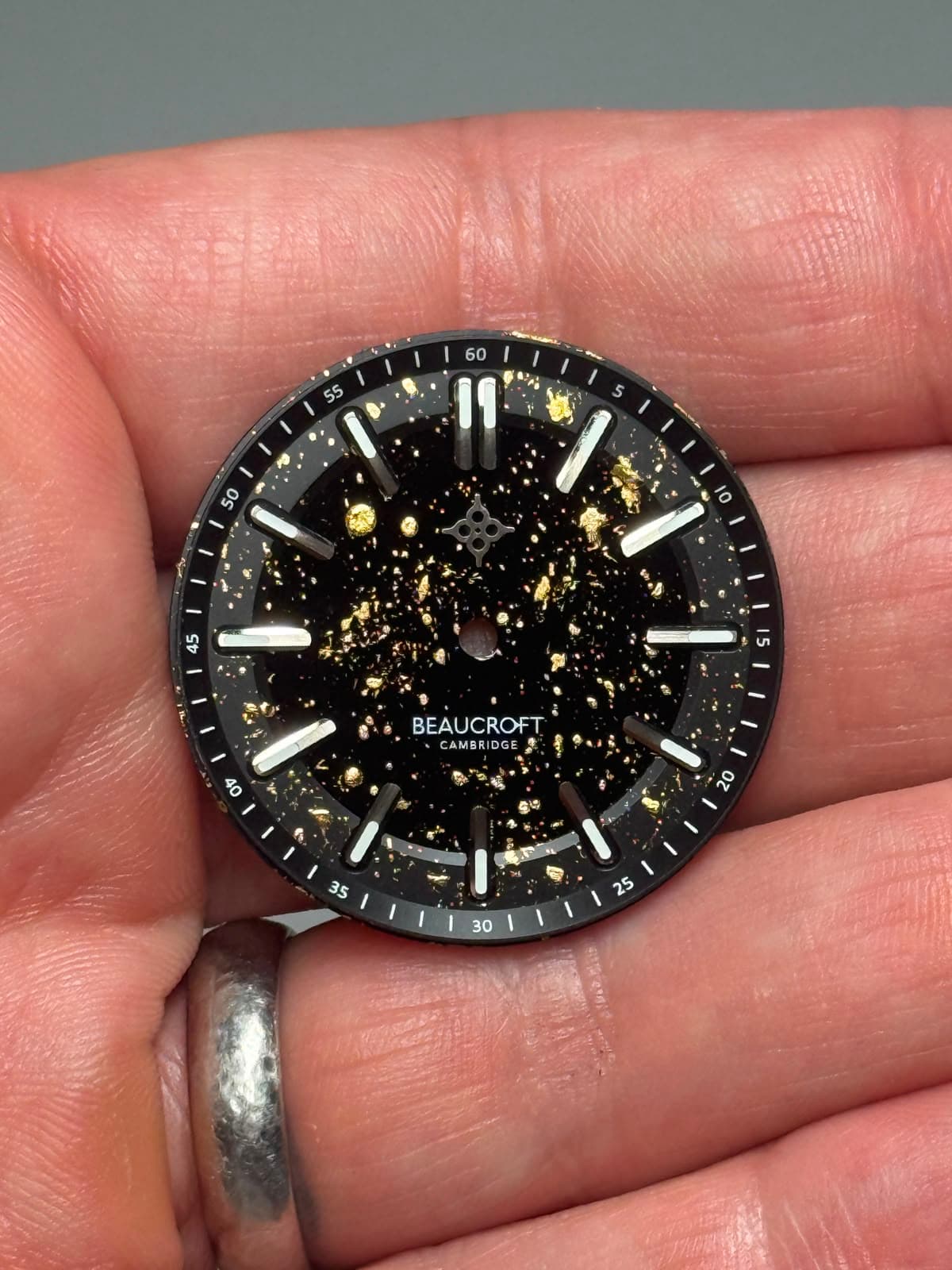 a black watch dial with gold leaf paint dots liberally applied all over it