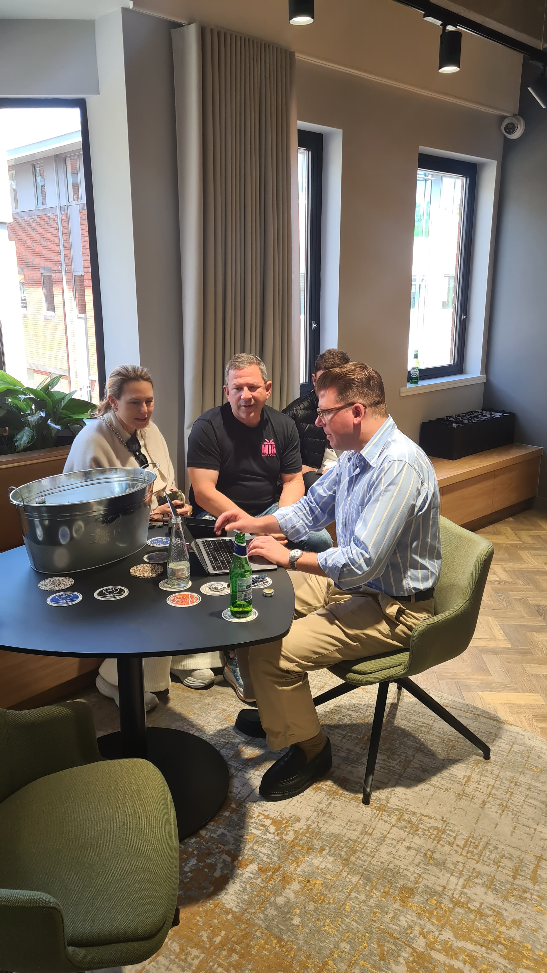 three people sit near a table with one one a laptop entering purchase details. green chairs black table beige carpet windows behind at Christopher Ward Maidenhead Showroom