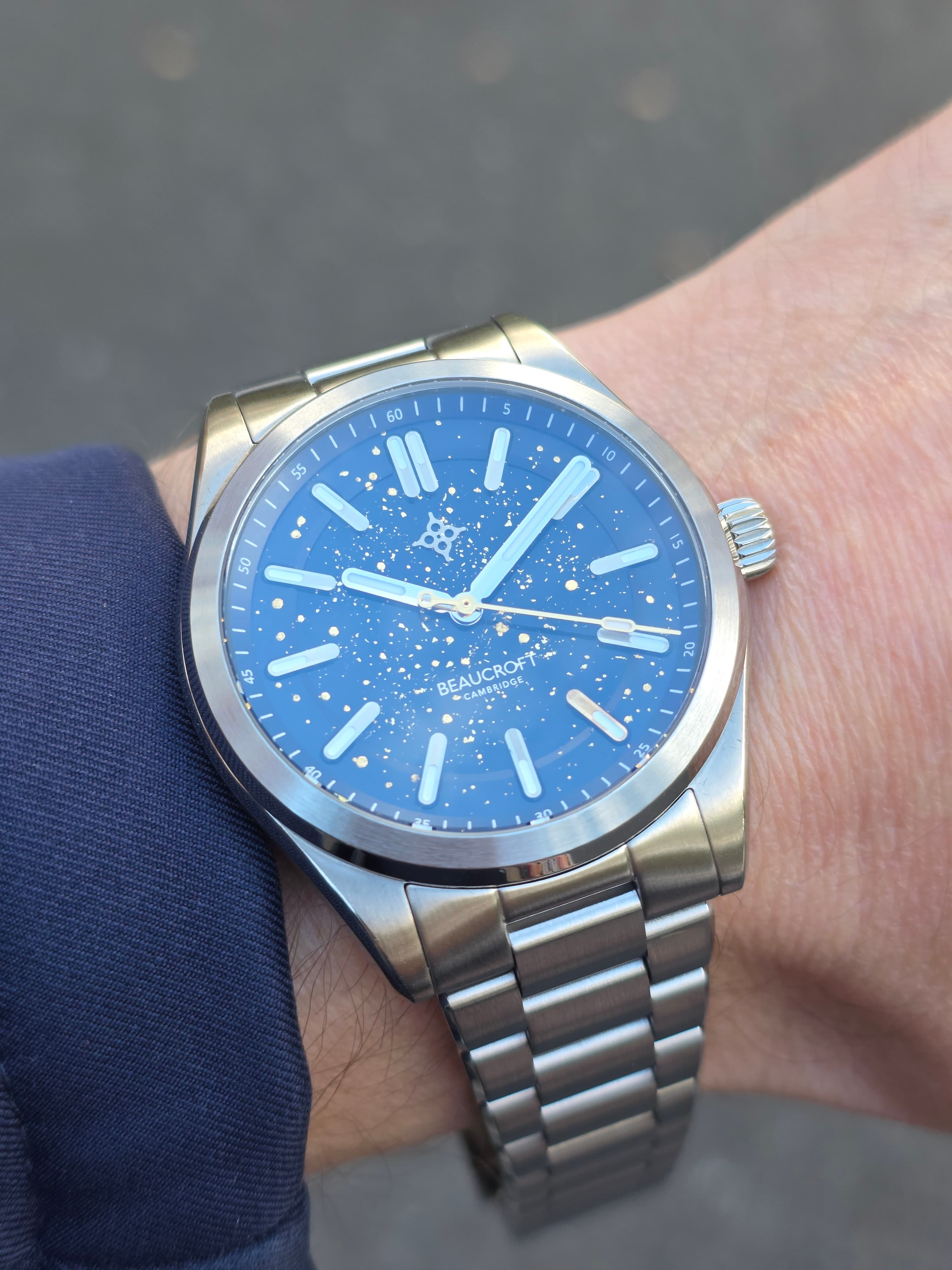 the beaucroft watch collectors club edition reflecting the sky but with the gold seconds hand and five index clearly visible with steel case and bracelet
