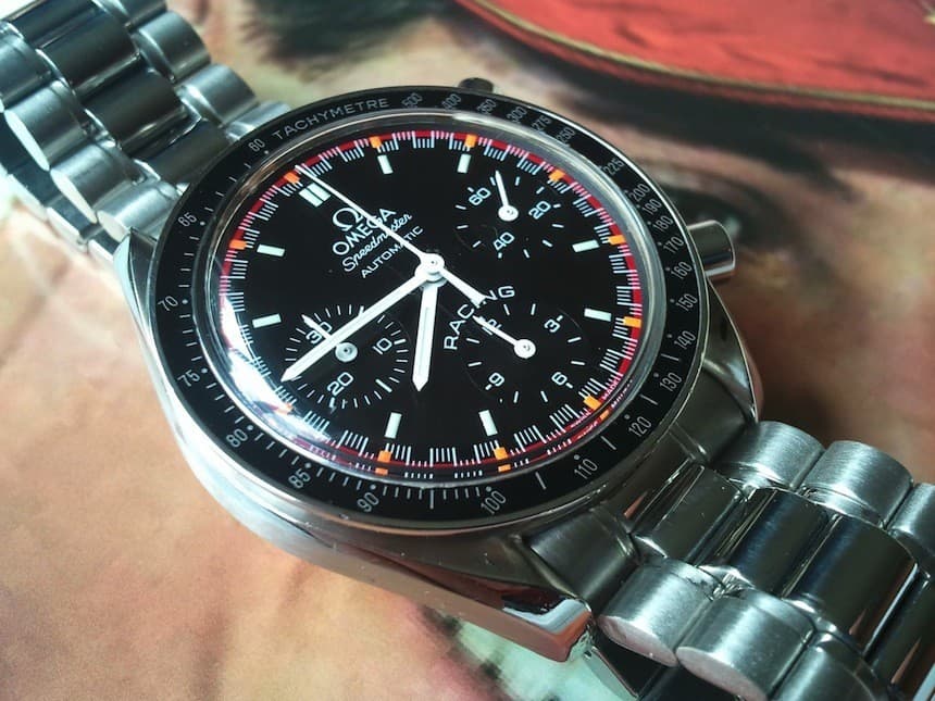 an omega speedmaster racing with a black dial and red an organe outer markgins and racing written above the 6 o'clock subdial in a steel case